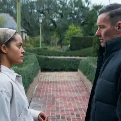 Due persone si guardano in un giardino curato, con siepi e un vialetto di mattoni. Le recensioni per "il maestro giardiniere" potrebbero descrivere scene come questa.