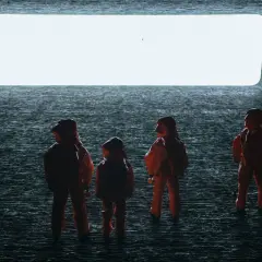Persone in tute arancioni osservano un'enorme apertura luminosa, evocando scene di "Arrival" e la sua spiegazione di un evento alieno.