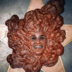 Volto umano emergente da una massa carnosa e pulsante, un'immagine disturbante tipica del **film body horror**.