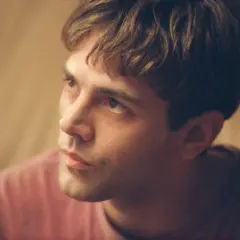 Primo piano di un giovane uomo con capelli castani e una maglietta rosa. Potrebbe essere Xavier Dolan fidanzato.