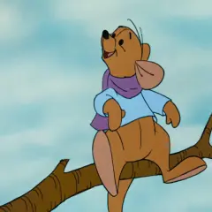 Winnie the Pooh, interpretato da Jim Cummings, siede su un ramo con una sciarpa viola e una camicia azzurra.