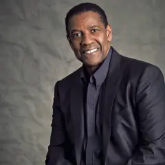 Ritratto di Denzel Washington, attore e doppiatore, con un sorriso caloroso e un abito scuro.