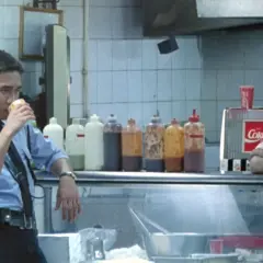 Un poliziotto sorseggia una bevanda, mentre una ragazza appoggia il mento sulle mani. Scena da "Hong Kong Express" con spiegazione implicita.