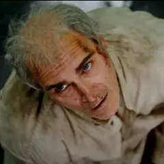 Un uomo con i capelli grigi e ferite sul viso, vestito di una camicia sporca, guarda in alto con espressione spaventata. Beau ha paura, spiegazione visiva.