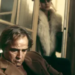 Marlon Brando pensieroso, sullo sfondo Maria Schneider in pelliccia. Scena iconica di "Ultimo tango a Parigi", la scena del burro.