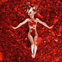 Una donna giace su un letto di rose rosse, un'immagine iconica che evoca la bellezza e la complessità di "American Beauty recensione".