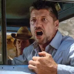 Fred Ward, attore noto per film d'azione, con espressione angosciata in auto. La sua causa morte è stata una malattia.