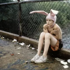 Bambino con cappello da coniglio seduto su un marciapiede sporco, un'immagine che evoca la trama di Gummo.