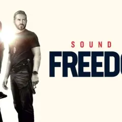 Un uomo abbraccia un bambino, mentre un altro uomo con una pistola guarda. Titolo: Sound of Freedom. Le recensioni lodano questo film.