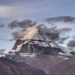 La montagna sacra spiegazione: il maestoso Kailash, coperto di neve, si erge tra nuvole scure e un cielo crepuscolare, simbolo di spiritualità e mistero.