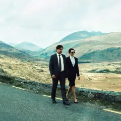 Coppia in abito cammina su strada panoramica, paesaggio montuoso. Un'immagine che evoca la recensione di "The Lobster".