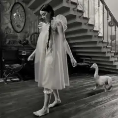 Bella Baxter, con un'aria sognante, cammina a piedi nudi in una casa d'epoca, accompagnata da un'oca e un cane.