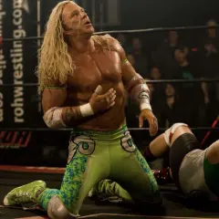 Randy the Ram, il wrestler dai lunghi capelli biondi, in ginocchio sul ring, guarda verso l'alto con espressione intensa.
