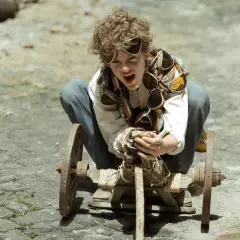 Un bambino con occhiali da aviatore intorno al collo, accovacciato su un carretto di legno, sembra pronto per l'ultima avventura da bambini.