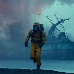 Uomo in tuta gialla corre su una spiaggia desolata, con una nave naufragata sullo sfondo. Le recensioni di Greenland descrivono scene apocalittiche simili.
