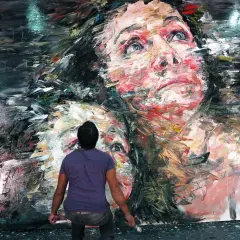 Un artista lavora a un ritratto espressionista di due volti, con pennellate audaci che ricordano lo stile di Annie Leibovitz.