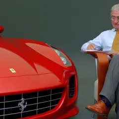 Un uomo d'affari con una cravatta gialla scrive appunti accanto a una Ferrari rossa, forse per le recensioni del film.
