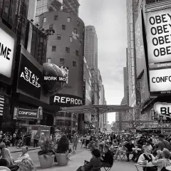 Times Square, un monito di messaggi che urlano "Consuma", "Obbedisci", "Conformati". Essi vivono significato: un'eco di controllo nella folla.