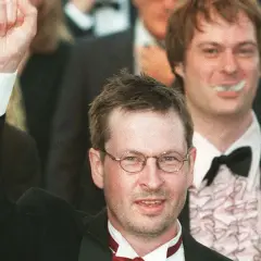 Lars von Trier, regista, alza il pugno in segno di vittoria, circondato da festeggiamenti.