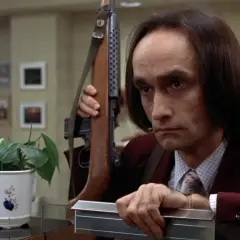 Un uomo con un fucile a tracolla, forse in una scena che ricorda il john cazale funeral, guarda intensamente.