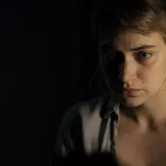 Primo piano di una giovane donna con sguardo preoccupato, in penombra. Un'immagine che evoca le atmosfere di "Vivarium", recensione.