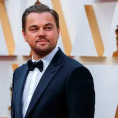 Leonardo DiCaprio, elegante in smoking, sorride con orgoglio, un'immagine che evoca i suoi numerosi premi vinti.