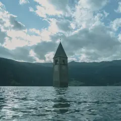 Torre sommersa nel lago, un'icona di Curon. Le recensioni la descrivono come un luogo suggestivo e malinconico, con montagne sullo sfondo.