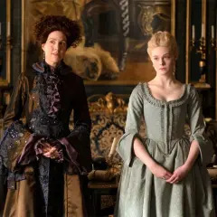 Due donne in abiti storici, una con capelli ricci e un vestito scuro elaborato, l'altra con capelli biondi raccolti e un abito verde chiaro. Le loro espressioni suggeriscono un momento di tensione, forse in attesa di grandi recensioni.
