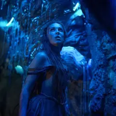 Una giovane donna con lunghi capelli scuri, vestita con abiti blu, guarda verso l'alto in una grotta illuminata da luci blu. La sua espressione è di stupore e meraviglia, quasi come se fosse una damigella in pericolo in un mondo alieno. La recensione d...