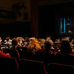 Pubblico in sala, immerso nell'oscurità, attende con il fiato sospeso i monologhi da brividi che stanno per iniziare sul palco illuminato.