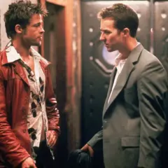 Il narratore di Fight Club, con la sua giacca rossa, parla con un uomo in completo grigio.