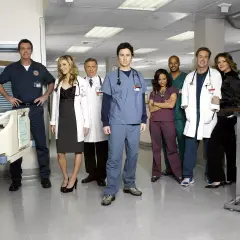 Un gruppo di medici ai primi ferri in scrubs e camici bianchi posa in un corridoio d'ospedale.