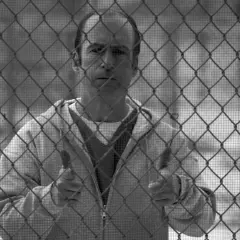 Un uomo dietro una rete metallica, con un'espressione pensierosa. Il suo gesto con i pollici in su suggerisce un "tutto bene" che contrasta con la sua situazione, evocando il **better call saul significato** di apparenza ingannevole.