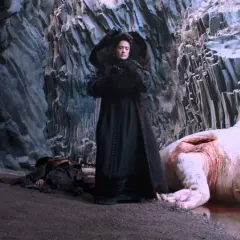 Una donna in nero osserva un mostro acquatico morto, con guerrieri al fianco. Scena da "Il racconto dei racconti recensione".