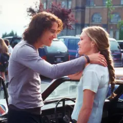 Il cast di "10 cose che odio di te" con Heath Ledger e Julia Stiles che si guardano sorridendo vicino a un'auto.