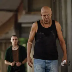 Due uomini, uno calvo e con un cerotto sul braccio, camminano in un ambiente urbano. Scena dal film "Adagio".