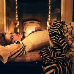 La favorita recensione: una donna con un abito a righe giace su un divano, illuminata da luci soffuse.