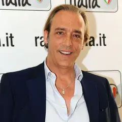 Luca Ward, noto per i suoi ruoli in film e programmi TV, sorride davanti a uno sfondo con il logo di Radio Italia.