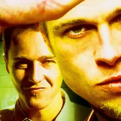 Primo piano di due uomini, uno con uno sguardo intenso, l'altro sorride. L'immagine evoca il **fight club significato** di ribellione e ricerca di identità.