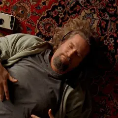 Un uomo con cuffie dorme su un tappeto persiano, accanto a un Walkman. Un'immagine iconica che evoca le recensioni de "Il Grande Lebowski".