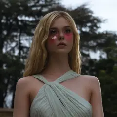 Ragazza con trucco glitterato e vestito verde pallido, un'immagine che evoca il significato di "The Neon Demon" e la sua ossessione per la bellezza.
