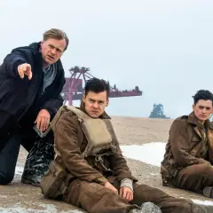 Il cast di Dunkirk, con Christopher Nolan che dirige i giovani soldati seduti sulla spiaggia.