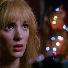 Kim, con sguardo preoccupato, è illuminata da luci colorate, un momento intenso con Edward mani di forbice.