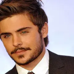Primo piano di Zac Efron giovane, con sguardo intenso e barba curata, indossa una giacca scura.