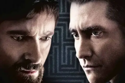 Primo piano dei volti intensi del cast di Prisoners, Hugh Jackman e Jake Gyllenhaal, con uno sfondo a labirinto.