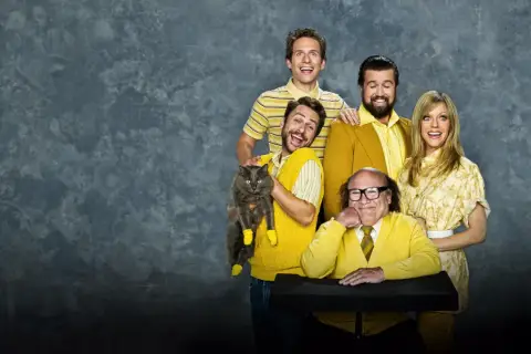 Il cast di "C'è sempre il sole a Philadelphia" posa sorridendo, con Charlie che tiene un gatto grigio con calzini gialli.