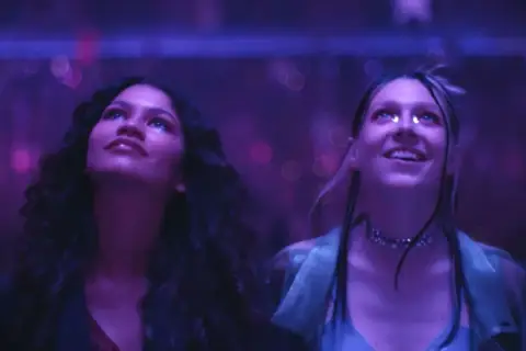 Due ragazze, immerse in luci viola, vivono un momento di pura **euforia 2**.