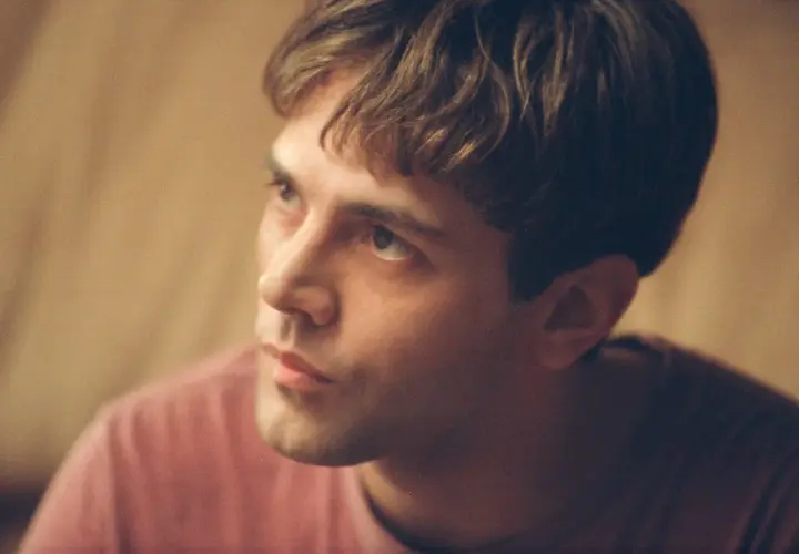 Primo piano di un giovane uomo con capelli castani e una maglietta rosa. Potrebbe essere Xavier Dolan fidanzato.