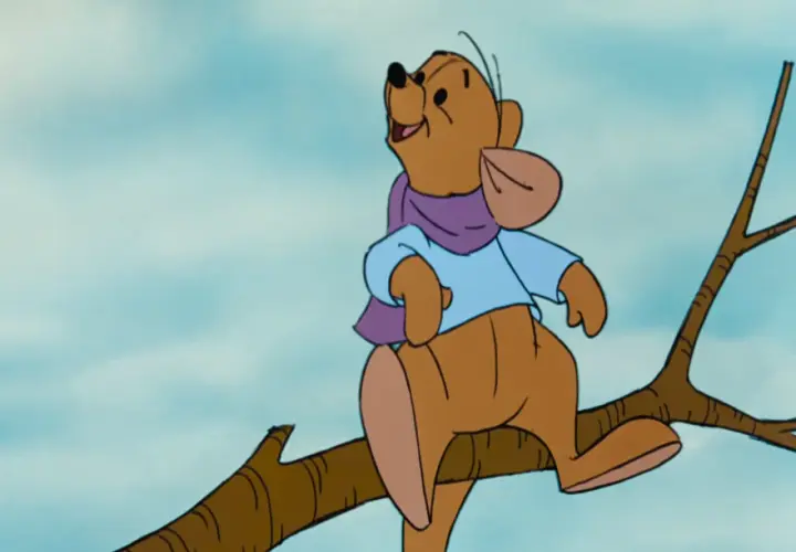 Winnie the Pooh, interpretato da Jim Cummings, siede su un ramo con una sciarpa viola e una camicia azzurra.