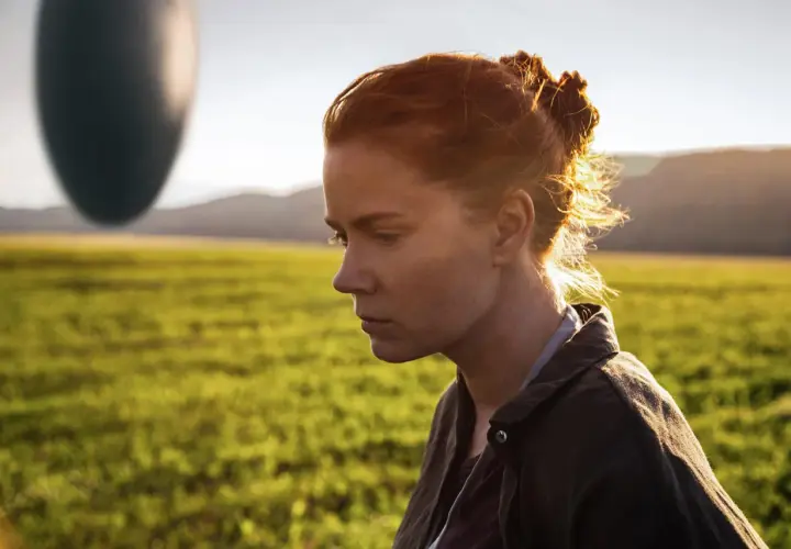 Donna con capelli rossi guarda un misterioso oggetto ovale fluttuante, simbolo dell'arrival linguaggio.